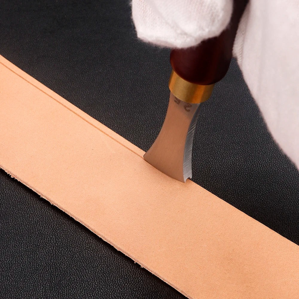 Leather edge creaser tool pressing a tan leather strip along a straight edge