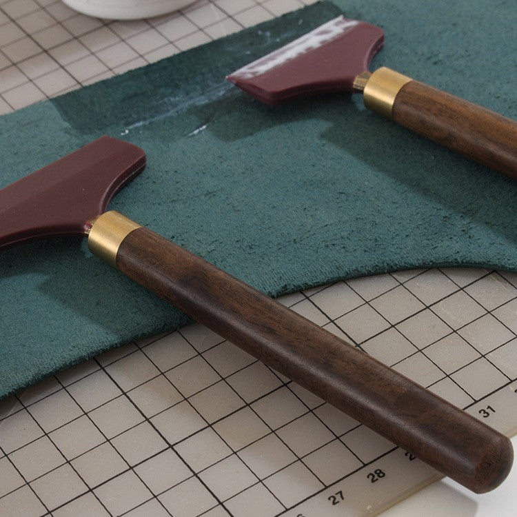 Glue spreader tool with brown wooden handle and maroon silicone scraper head