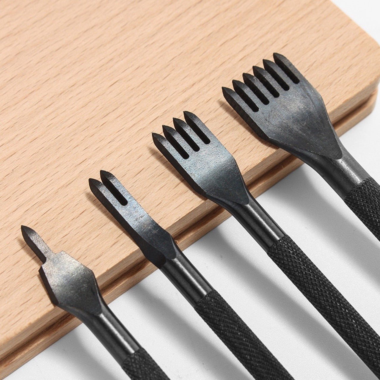 Leather chisels with black textured round handles and forked blades on wood