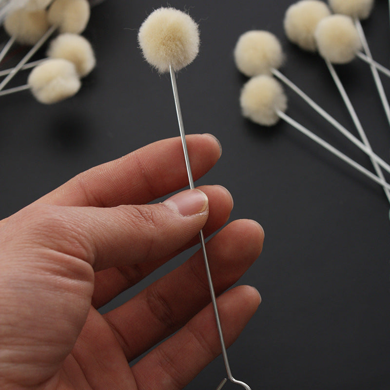 Hand holding wool dauber ball applicator with beige wool head on metal rod