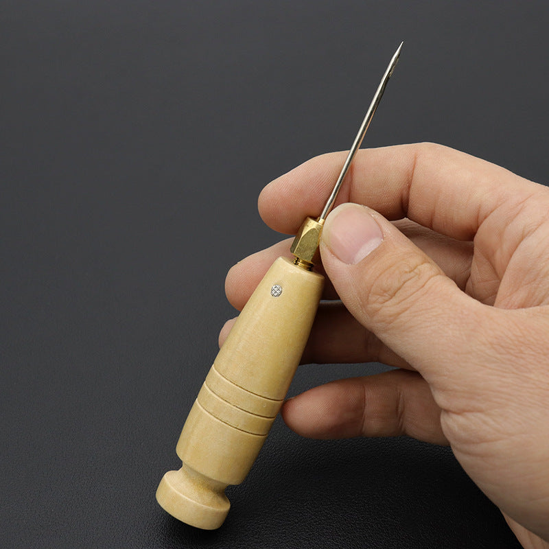 Wood-handled sewing awl held in hand with pointed needle tip upward