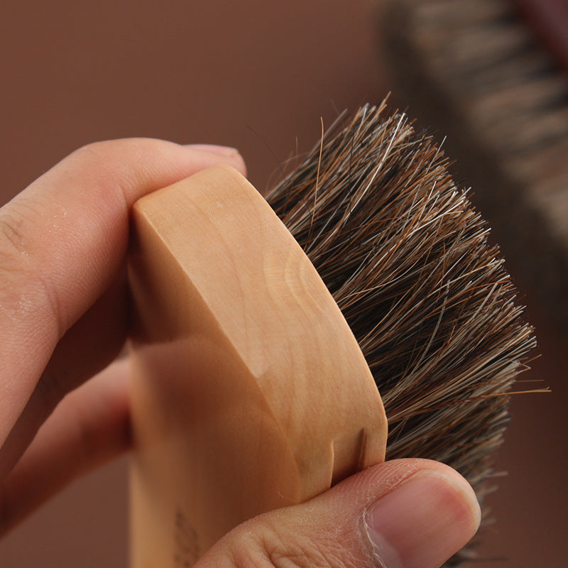 Handheld leather horsehair brush with light wooden handle and dense dark bristles