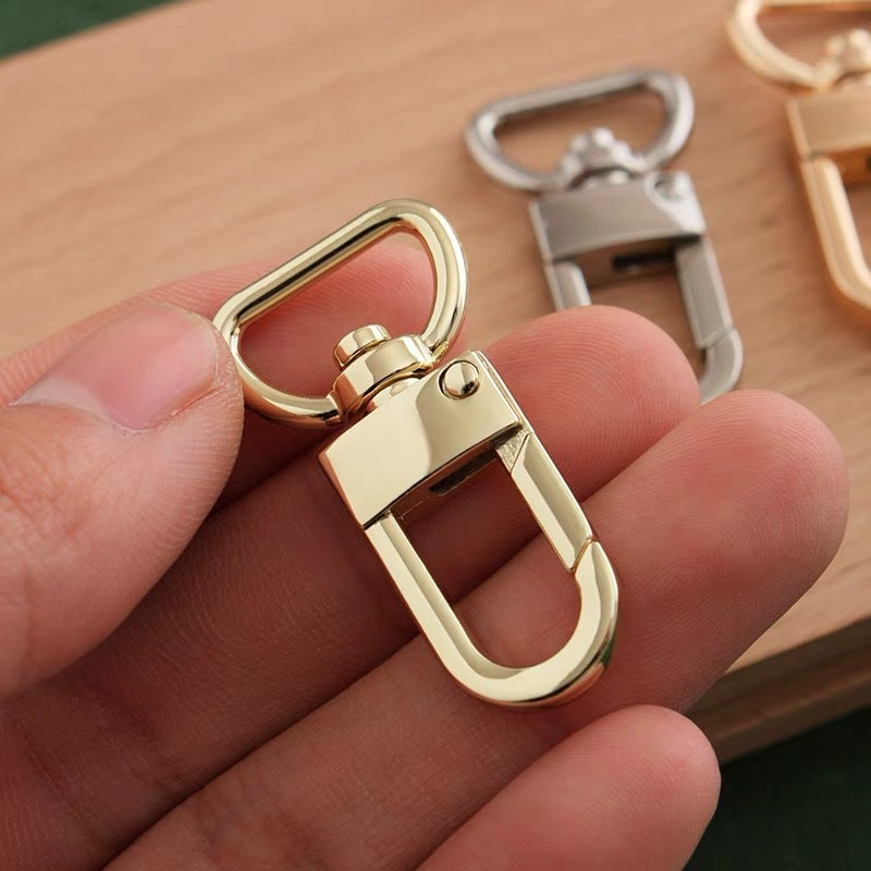 Gold metal swivel snap hook clasp with ring, close-up held between fingers.