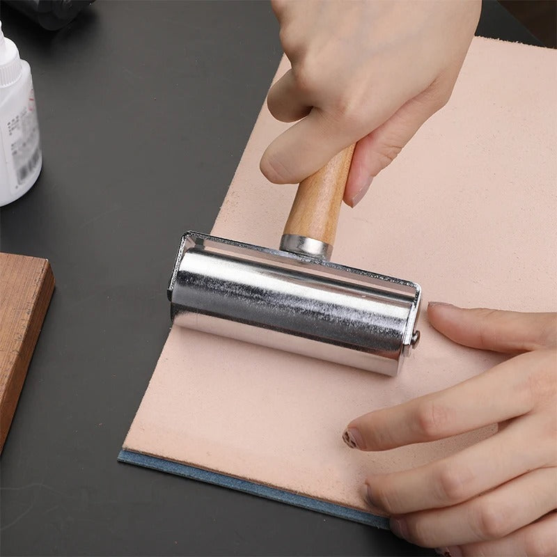 Leather roller press with light wood handle and chrome metal roller, in use on leather