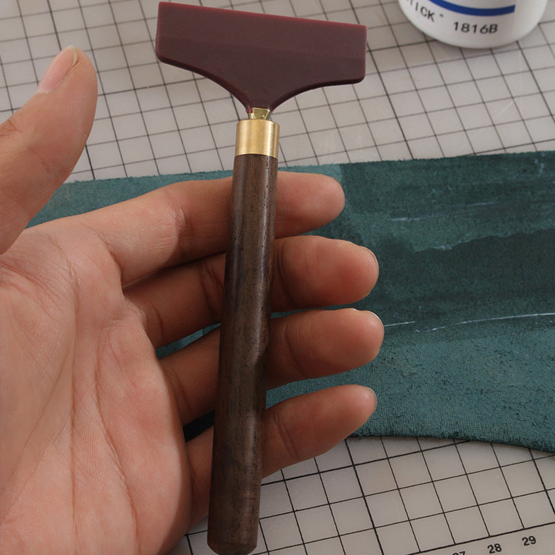 Glue scraper handle in hand, brown wood with brass collar and maroon silicone blade