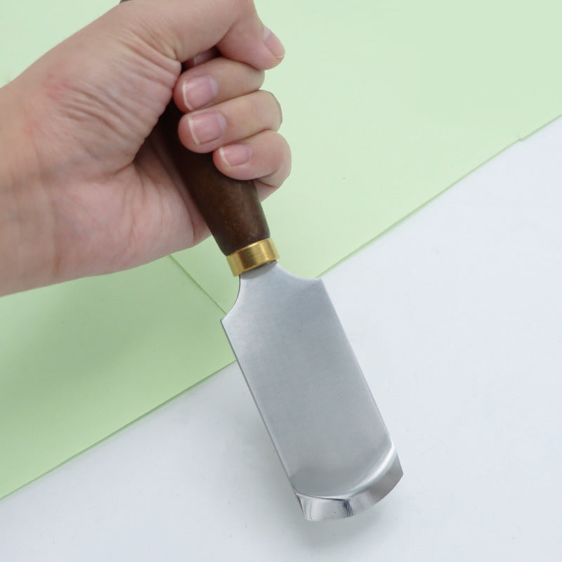 Leather skiving knife held in hand with dark walnut handle and curved steel blade