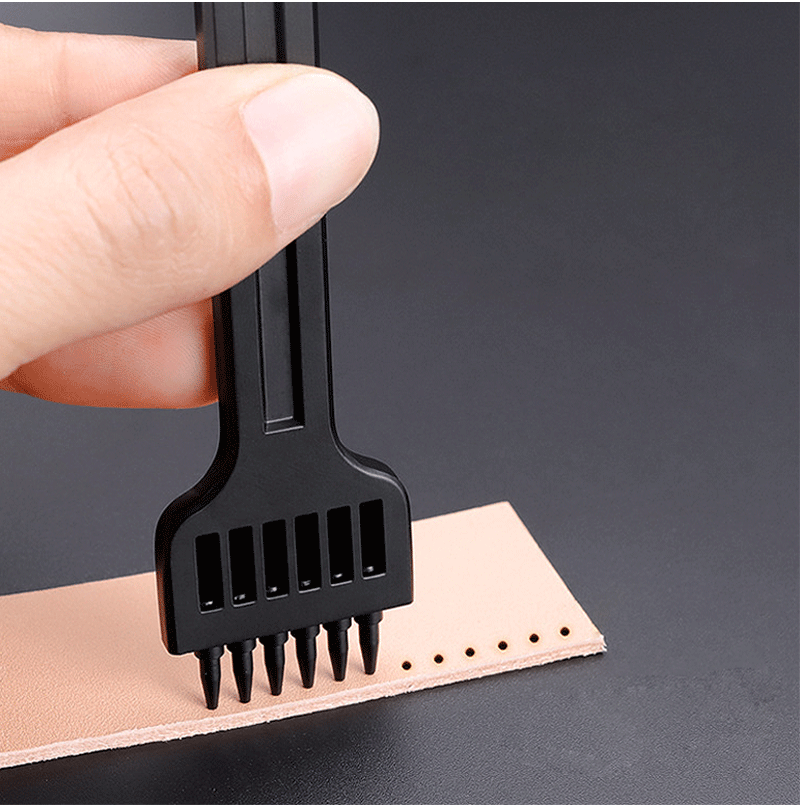 Hand presses a black leather hole punch onto tan material with pinned tip