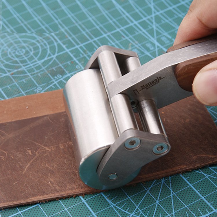 Leather roller tool pressing down a leather strip; hand holds wooden handle